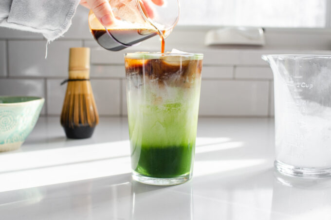 Layered iced matcha latte with espresso shot pouring over cream